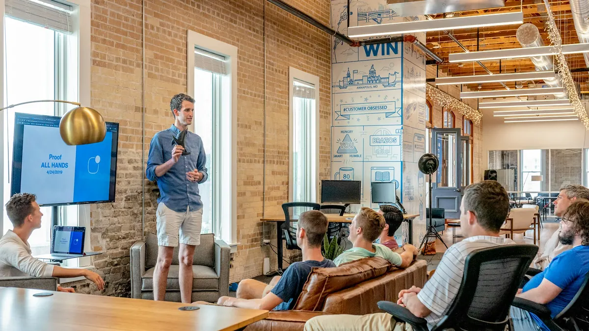 A team gathered in a bright brick-walled office as a colleague presents